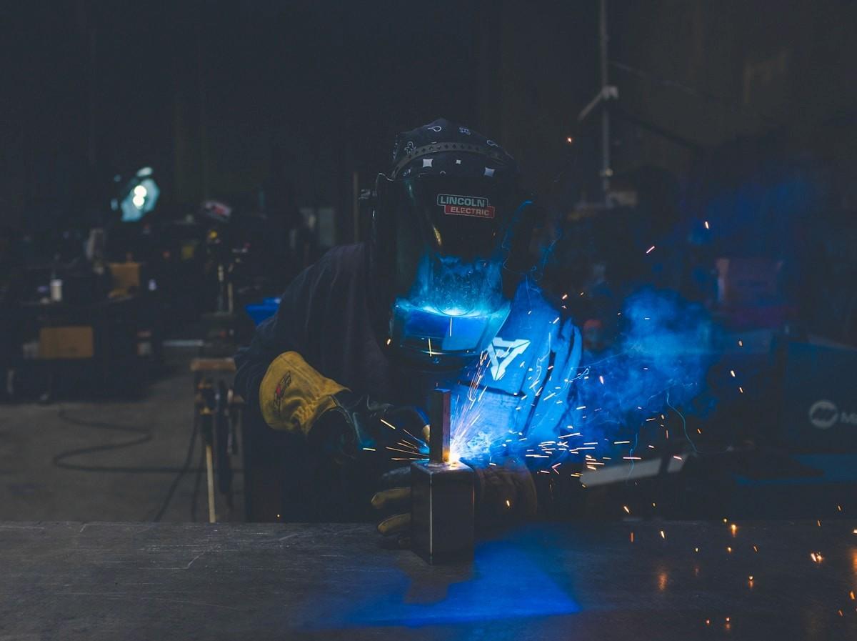 A welder at work, sparks and blue light around the weld